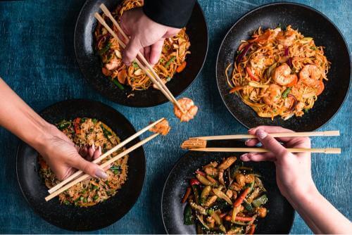 4 hands holding chopsticks over food on plates 